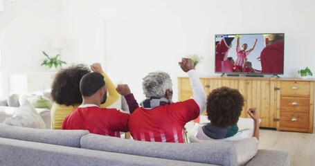 Wall Mural - African american family watching tv with diverse male soccer players playing match on screen