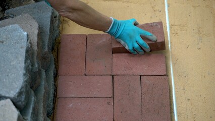 Overhead closeup of womans hand putting brick pavers onto a sand base for a patio construction.