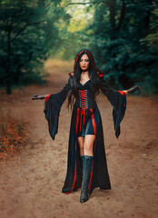 Fantasy halloween woman witch walks in summer nature green forest trees. Gothic girl sexy face, black red dress creative design carnival costume old vintage style, hood on head. Hands in ashes paints.