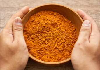 Wall Mural - man hand holding a pile of ground turmeric powder or curcumin powder in wood plate on wooden table background. turmeric or curcumin powder background