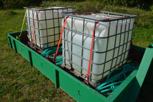 Two Plastic Containers In A Metal Cage. Full Of Water For Watering Or Drinking Livestock In Hot Weather. The Car Pulls The Container Onto The Rear Wheel. Arrange A Delivery Of Chemicals Or Fuel. Agro 