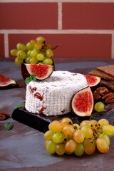 Fresh homemade cheese with dried tomato, fenugreek and herbs served on wooden board with fig, grape, pecan nuts and crispbread