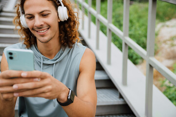 Wall Mural - Young long-haired athletic smiling man in headphones using phone