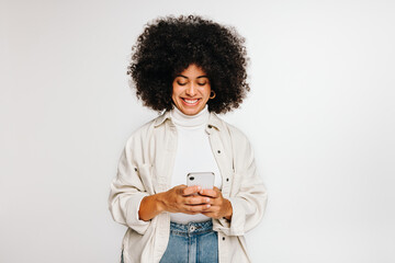 Wall Mural - Woman with curly hair smiling at her smartphone screen in a studio