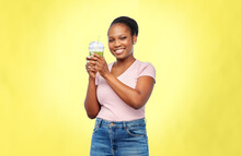 Diet, Healthy Eating And Detox Concept - Happy Smiling Young African American Woman Drinking Green Vegetable Juice Or Smoothie From Plastic Cup With Paper Straw Over Illuminating Yellow Background