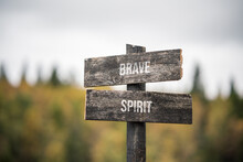 Vintage And Rustic Wooden Signpost With The Weathered Text Quote Brave Spirit, Outdoors In Nature. Blurred Out Forest Fall Colors In The Background.
