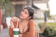 An attractive lady wearing a brown puffed long sleeved dress sits outside the cafe with her cold drink.