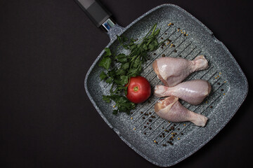 Wall Mural - Chicken legs in a grill pan on a black background. Fresh raw chicken legs.