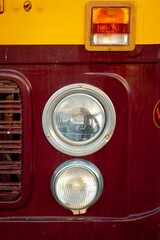 Sticker - Vertical closeup of a detail of a headlight of a red and yellow vintage bus