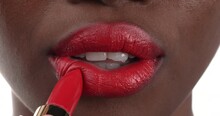 Close up view of a black woman applying red lipstick to her lips then smiling. Isolated on a white background.