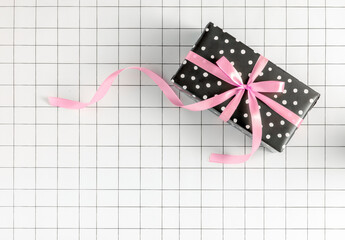 2023 New Year b&w minimal concept with polka dot wrapping paper gift box with pink ribbon bow on grid background. Christmas celebration, birthday, women's day aesthetic. Shopping, party, holiday idea.