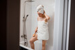 © bondvit - Young beautiful woman in white towel doing body lymphatic drainage massage with dry wooden brush with natural bristles in bathroom at home. Anti-cellulite exercises