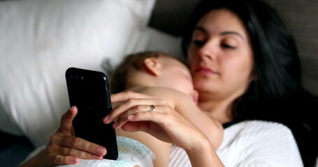 Wall Mural - Candid mother looking at smartphone while baby infant naps