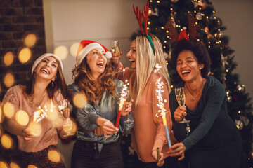 Wall Mural - Multiethnic Female Friends Playing With Sparklers And Making Toast As During Christmas Home Party