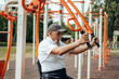 © sushytska - Persistent mature man with disabilities doing fitness exercises on outdoor simulator, pumping muscles and training endurance, rehabilitation, work on oneself, the desire to be healthy