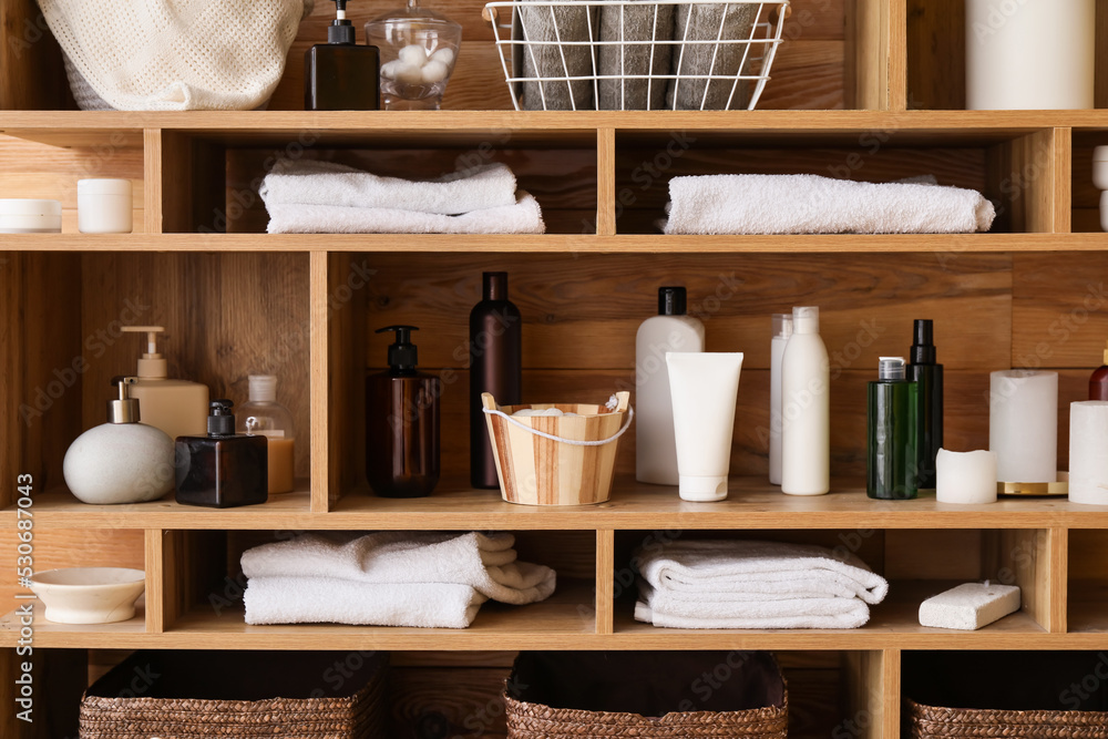 Different bath accessories on shelf unit near wooden wall, closeup