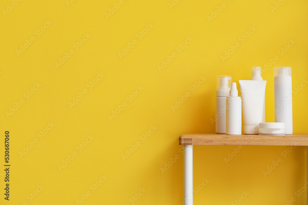 Bath accessories on wooden shelf near yellow wall