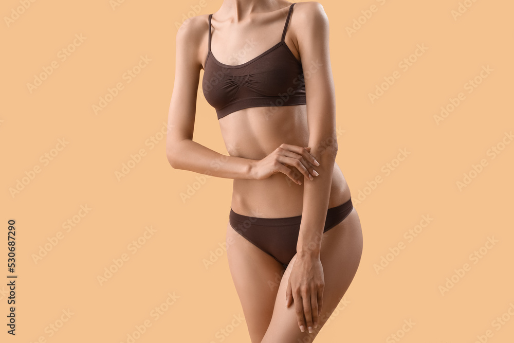 Slim young woman in underwear on beige background