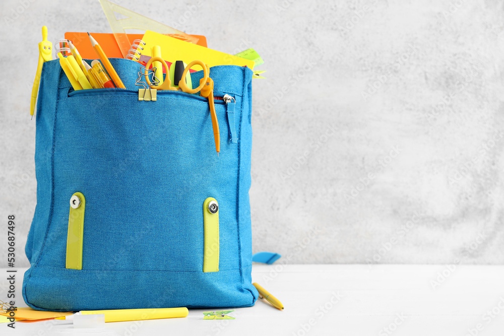 Blue backpack with school stationery on light background