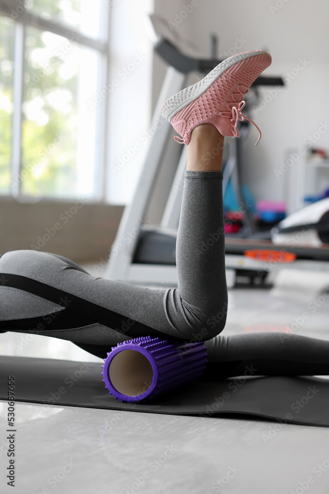 Young woman exercising with foam roller in gym, closeup