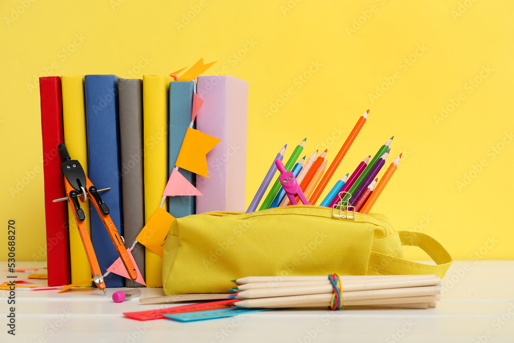 Pencil case with school stationery and books on table against yellow background