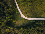 Fototapeta Uliczki - Top down aerial drone view of the road in mountain range trough the trees and forest and car parked wild travel rural vacation and nature concept background