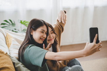 Poster - Two asian young women happy smiling and taking selfie on couch in living room at home