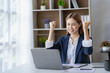 © ArLawKa - Adorable Asian businesswoman enjoying success working in the office with her laptop and company financial accounting documents.