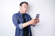 © Reezky - Surprised Asian man wearing navy blue shirt pointing at his smartphone, isolated by white background