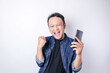 © Reezky - A young Asian man with a happy successful expression wearing navy blue shirt and holding smartphone isolated by white background