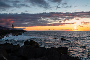 Watching the sunset from the port of Puerto de la Cruz, Tenerife, Canary Islands, Spain, Europe. View of the horizon of Atlantic Ocean. The sun is reflecting in the calm sea. Vibrant clouds in the sky