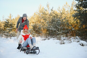 A side view of a happy couple having fun while sliding downhill together over snowy slope using a sled