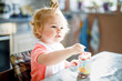 Adorable baby girl eating from spoon vegetables or fruit canned food, child, feeding and development concept. Cute toddler, daughter with spoon sitting in highchair and learning to eat by itself.