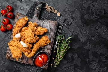 Wall Mural - Dip fried Breaded chicken breast strips with tomato ketchup on a wooden board. Black backgrund. Top view. Copy space