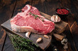 Prime T-bone beef meat steak, raw porterhouse steak on butcher board with herbs. Wooden background. Top view