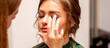 The hand of a makeup artist applies eye shadow on the eyelid of a young Caucasian woman with fingers in a beauty salon