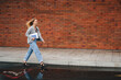 © Strelciuc - Side view portrait of a woman student walking outdoors against brick wall background, holding white laptop while smiling. Urban background. Youth lifestyle