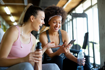 Wall Mural - Happy fit women, friends smiling, talking and taking photos after work out in gym. Social media.