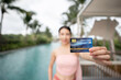Woman holding credit card in hand by the pool, shopping online on vacation.