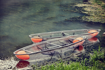 Two transparent boats on the lake near the shore .