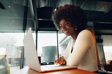 Smiling young african woman sitting with laptop in cafe