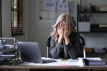 Tired and stressed young asian woman sitting at her working place..