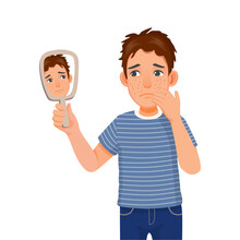 Anxious Young Man Holding Mirror Looking At Acne Spot Pimples On His Face