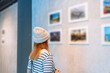 © Kiattisak - Woman visiting art gallery her looking pictures on wall watching photo frame painting at artwork museum people lifestyle concept.