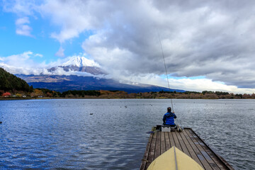 Wall Mural -  A Man Sit and Fishing Alone on wooden bridge at Kawaguchiko Lake in Japan during Sunset with Fuji Mountain Background