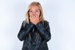 © Jihan - Stunned beautiful caucasian blonde little girl wearing biker jacket and glasses over white background covers mouth with both hands being afraid from something or after hearing stunning gossips.