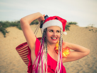 Wall Mural - Happy middle aged attractive brunette woman in red swimsuit and Santa hat having fun on the coast. Christmas holiday vacation and travel concept.