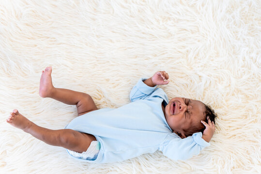 Portrait images of half Nigeria half Thai, 1-month-old baby newborn son, lying on a white bed and is crying, to infant and family concept.