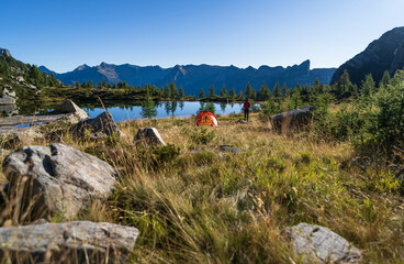 Fototapete - Hiker beside her red tent in the mountains of Ticino on a beautiful morning in the summer.