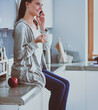 © lenets_tan - Woman using mobile phone sitting in modern kitchen.